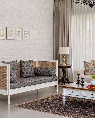 White cane-backed settee with floral cushions against whitewashed brick wall, framed art above