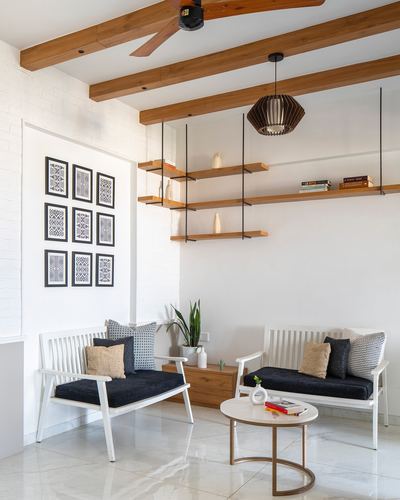 White living room with wooden beams, floating shelves, two navy benches and marble floor