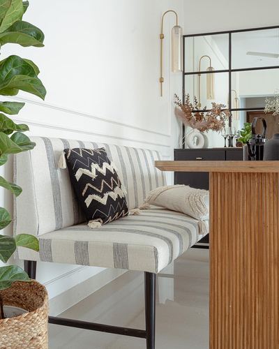 Striped bench with patterned cushions beside a fluted wood console and mirrored wall