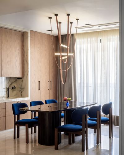 Dining room with blue velvet chairs, dark wood table, and a sculptural pendant light against wooden cabinetry