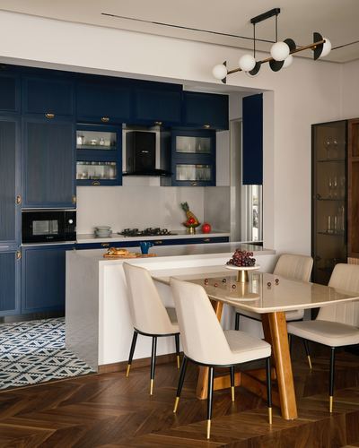 Navy blue kitchen with white island opening to dining table with cream chairs and herringbone wood floor