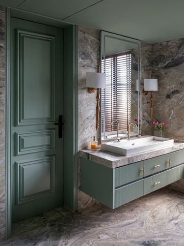 Sage green paneled door beside a marble bathroom with floating fluted vanity and brass fittings