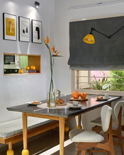 Dining nook with dark stone table, wooden bench, gallery wall, and yellow wall lamp near window