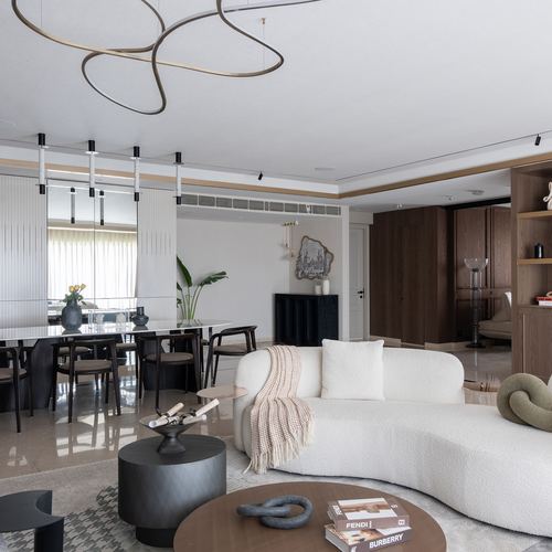 Open living room with curved white boucle sofa, sculptural pendant light, and dining area beyond