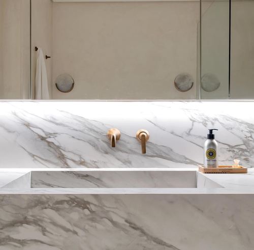 Marble bathroom vanity with brass wall-mounted faucets and backlit mirror
