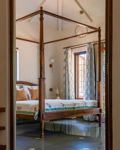 View through doorway of a wooden four-poster bed beneath a pitched ceiling with a leaded glass window.