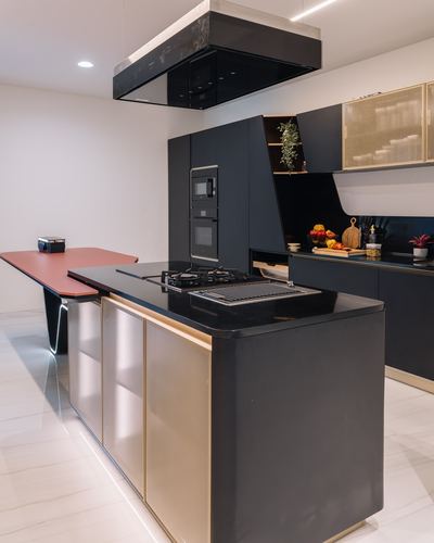Black and gold kitchen island with hob under a suspended black hood, terracotta cantilevered table beside it