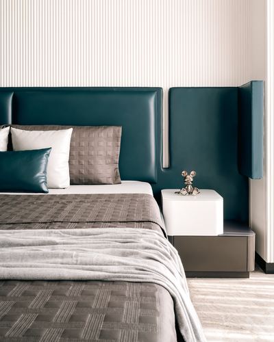 Bedroom with tall teal leather headboard, grey quilted bedding, and glossy white nightstand with a small figurine.