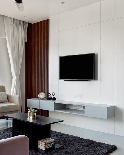 Minimalist living room with wall-mounted TV, floating grey unit, and fluted wood panel accent.