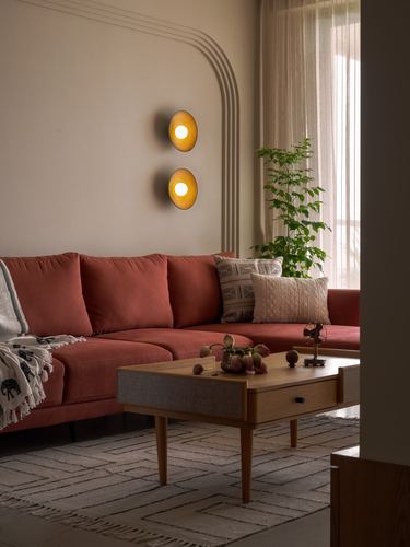 Terracotta sofa beneath arched wall niche with two glowing circular sconces, wood coffee table in foreground