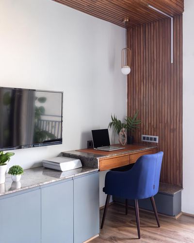 Study nook with fluted wood paneling, built-in desk, blue chair, and wall-mounted TV over stone-topped cabinetry