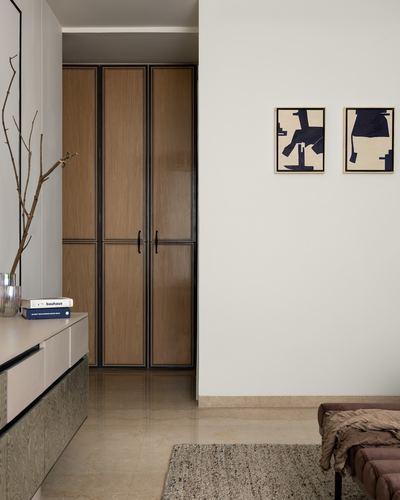 Foyer with wood wardrobe framed in black metal, console table, and two abstract framed prints on cream wall