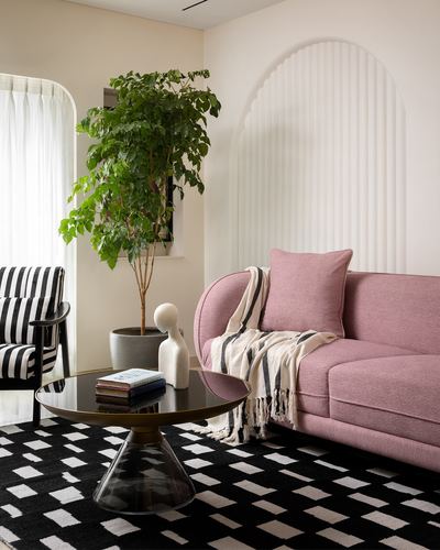 Pink curved sofa beside fluted arch niche with black and white patterned rug in Mumbai apartment