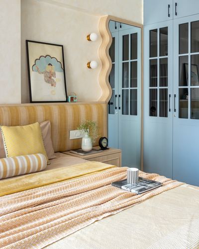 Bedroom corner with mustard striped headboard, wavy mirrored niche, and powder blue glass wardrobes