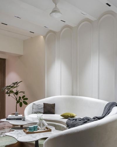Curved white sofa against arched panelled wall with marble coffee tables in neutral living room