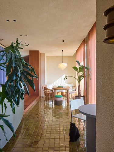 Long corridor with glossy ochre tile floor leading to dining nook, black cat sitting mid-frame
