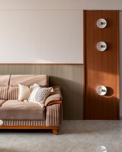 Channel-tufted pink sofa beside fluted wall panel and wood-clad column with round sconces