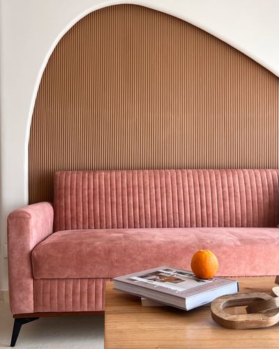 Pink channel-tufted sofa against an arched fluted wood-panelled niche with a wooden coffee table