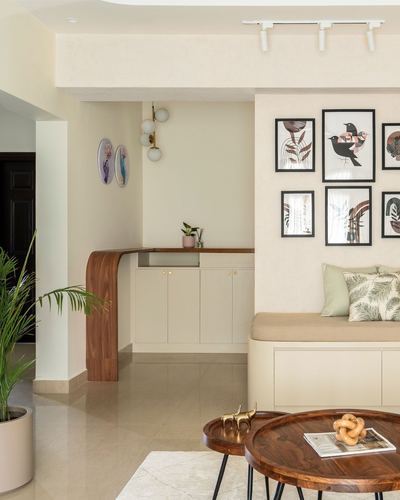 Neutral-toned living space with curved wood counter, gallery wall, and cushioned bench seating