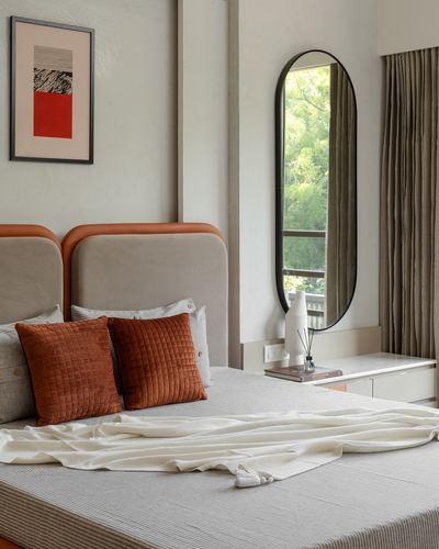 Bedroom with curved leather-edged headboard, terracotta cushions, and tall oval mirror by window