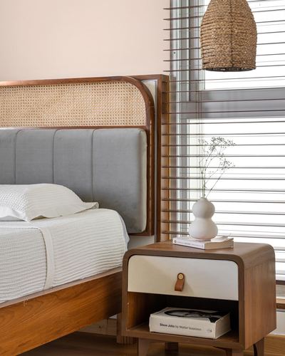 Bedroom corner with cane headboard, grey upholstered panel, wooden nightstand and woven pendant light by window