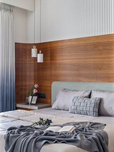 Bedroom with wood veneer headboard wall, fluted plaster above, pendant lights over a stone bedside ledge