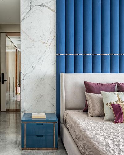 Bedroom corner with blue channel-tufted headboard wall, marble pilaster, and blue lacquered nightstand