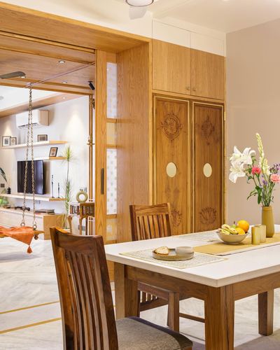 Dining table beside carved wooden wardrobe with brass inlay, view through to living room with swing