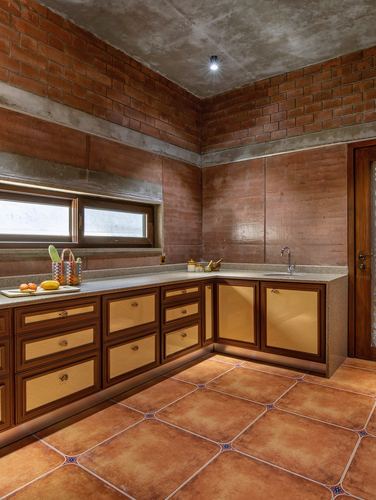 L-shaped kitchen with exposed brick walls, terracotta tile floor and cane-panelled wooden cabinets