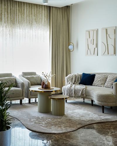 Beige living room with curved sofa, armchairs, nesting round tables and sculptural wall art