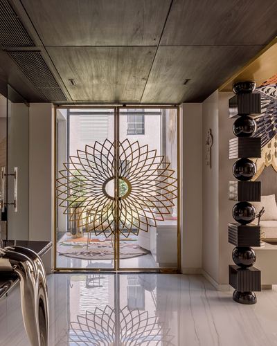 Foyer with gold sunburst grille doors, wood ceiling, and black sculptural totem beside marble floor
