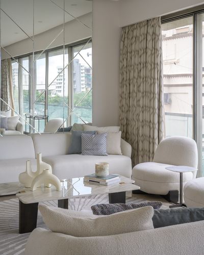 Cream living room with boucle sofas, marble coffee table, and mirrored geometric wall overlooking city view
