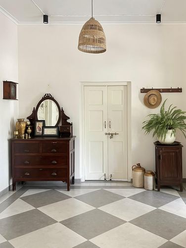 Foyer with checkered tile floor, antique wooden dresser, mirror, and cane pendant light