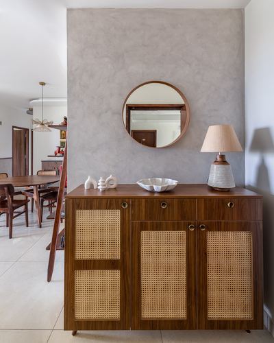 Wood and cane sideboard with round mirror and lamp against a textured plaster wall in a foyer