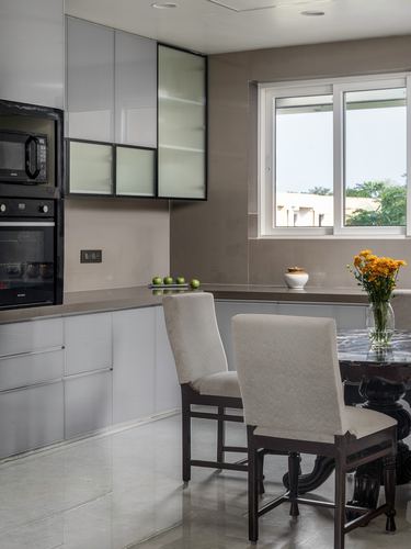 Modern kitchen with grey cabinetry, glass-front uppers, window, and a carved wood dining table with upholstered chairs