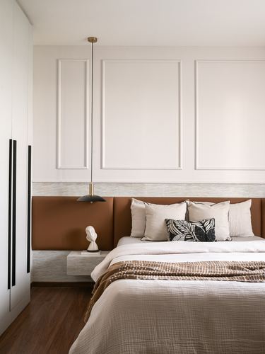 Bedroom with paneled wall, brass pendant light, rust upholstered headboard and floating nightstand