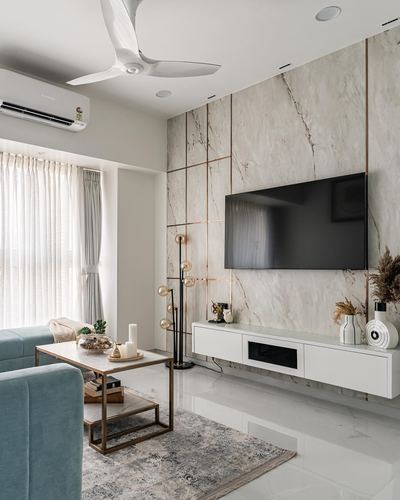 Minimalist living room with veined stone TV wall gridded in brass, blue sofa, and floating console