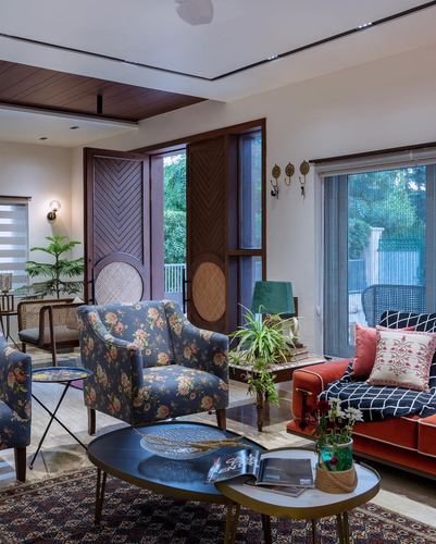 Living room with floral armchair, red velvet sofa, carved wooden doors opening to greenery
