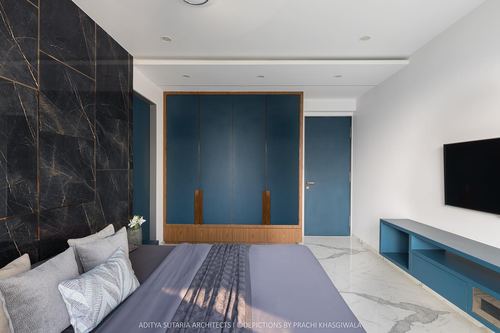 Contemporary bedroom with dark stone accent wall, blue wardrobe, and marble flooring