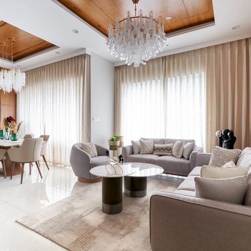 Neutral living room with grey sofas, round marble-look tables, and a wood-clad ceiling with chandelier