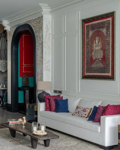 White paneled living room with framed tapestry, cushioned sofa, and arched doorway to red vestibule