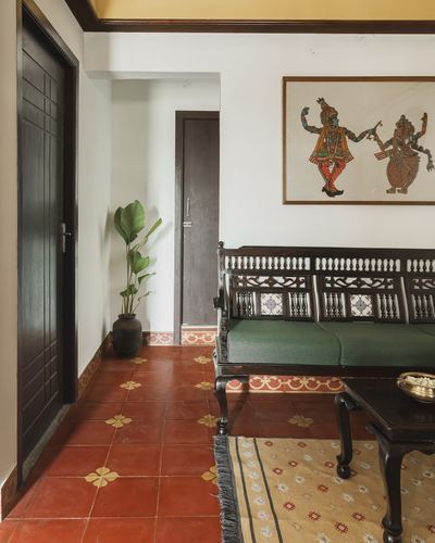 Traditional Indian living room with carved wooden settee, green cushions, folk painting, and red Athangudi tile floor