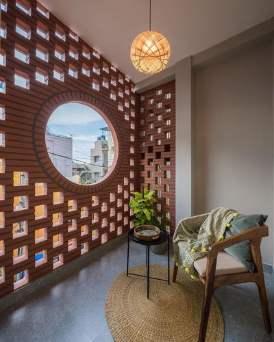 Balcony corner with perforated terracotta jaali wall, round window, cane chair and rattan pendant light