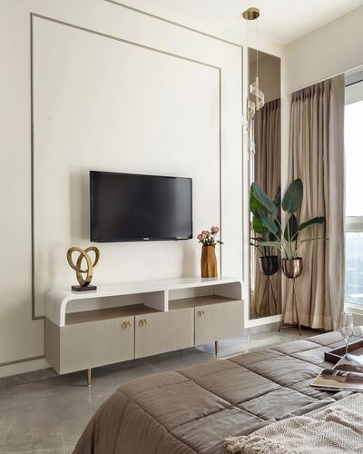 Beige bedroom with tv console, brass sculpture, plants, and quilted bed in soft daylight