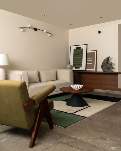Living room with olive bouclé armchair, cream sofa, wooden sideboard and layered geometric rug