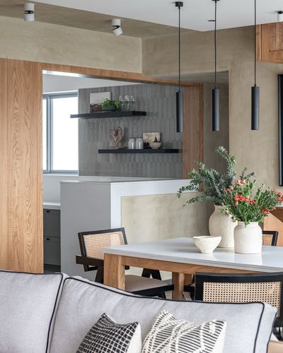 Dining table with cane chairs beneath black pendant lights, wood-framed kitchen niche behind