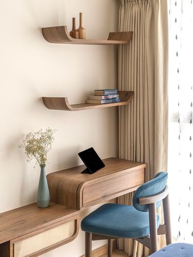 Corner study nook with curved wooden shelves, desk, tablet, and teal upholstered chair against curtained window