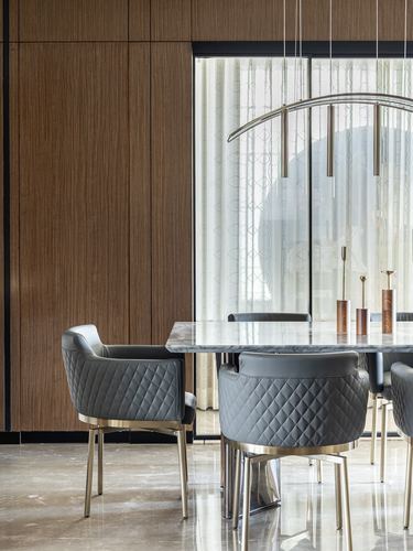 Dining area with grey quilted chairs, marble-look table, and brass arc pendant against wood paneled wall