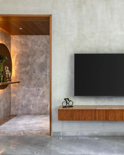 Living room with textured wall, TV on fluted wood console, adjoining marble alcove with glowing niche