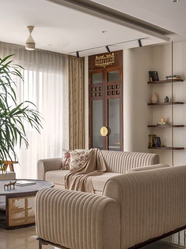 Beige channel-tufted sofas facing a wooden cabinet with brass detailing and floating shelves